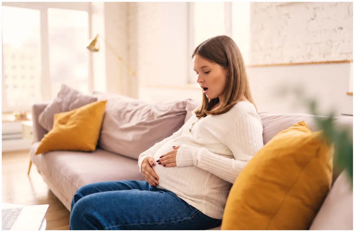 Femme enceinte installée chez elle, les mains posées sur son ventre